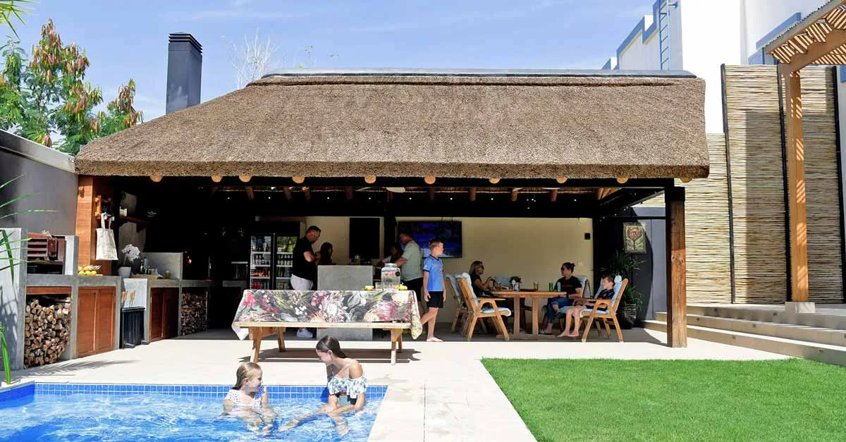 A beautifully designed outdoor living room with a thatched roof, comfortable seating, and vibrant greenery surrounding the space.